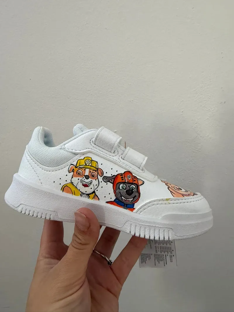 Hand holding a child's trainer painted with Paw Patrol characters.